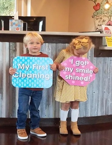 Two toddlers holding signs after their first dental visit at The Kid’s Place in Boerne